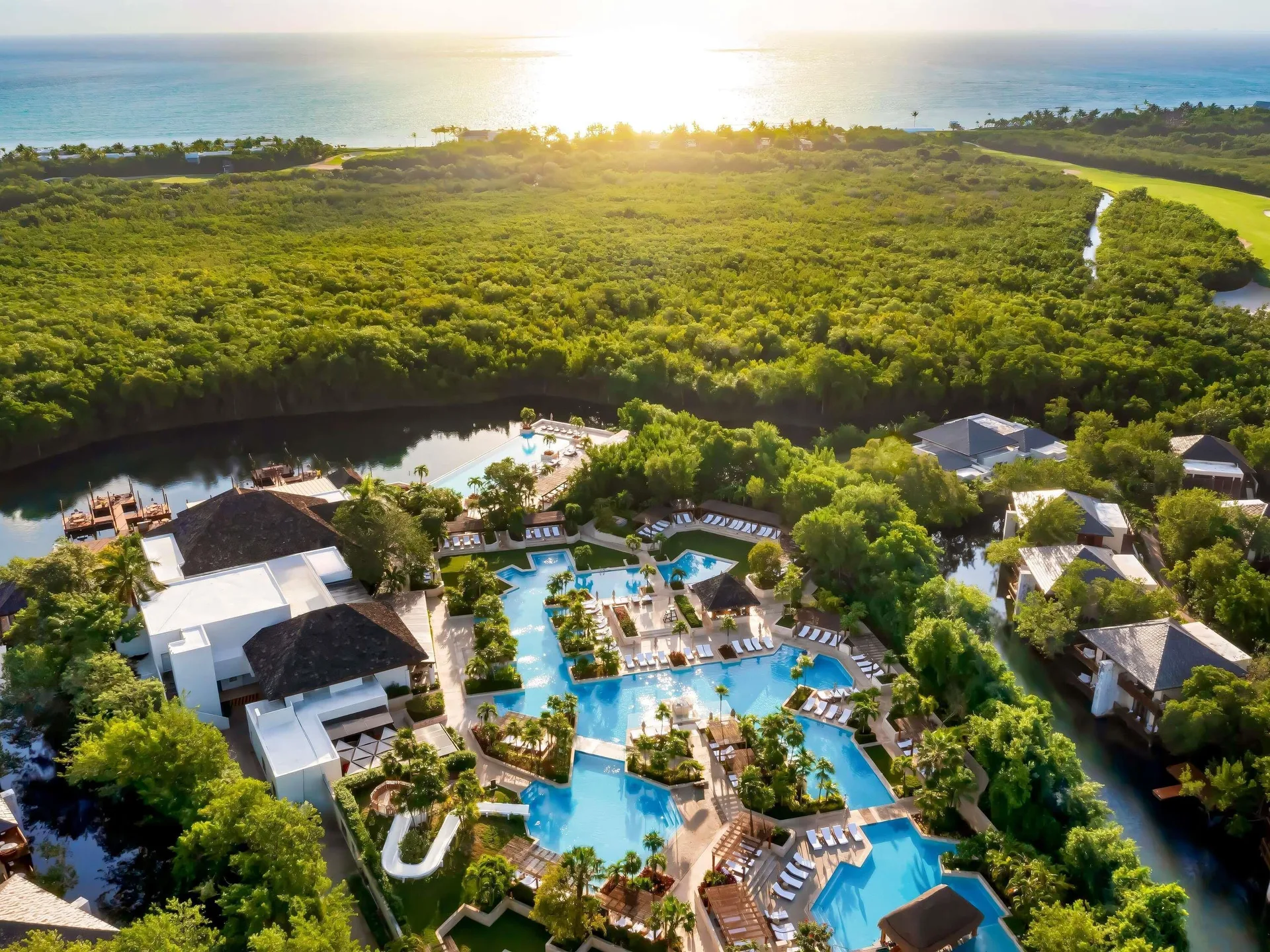 Aerial view of Fairmont Mayakoba pools, waterways, forest, and ocean beyond.