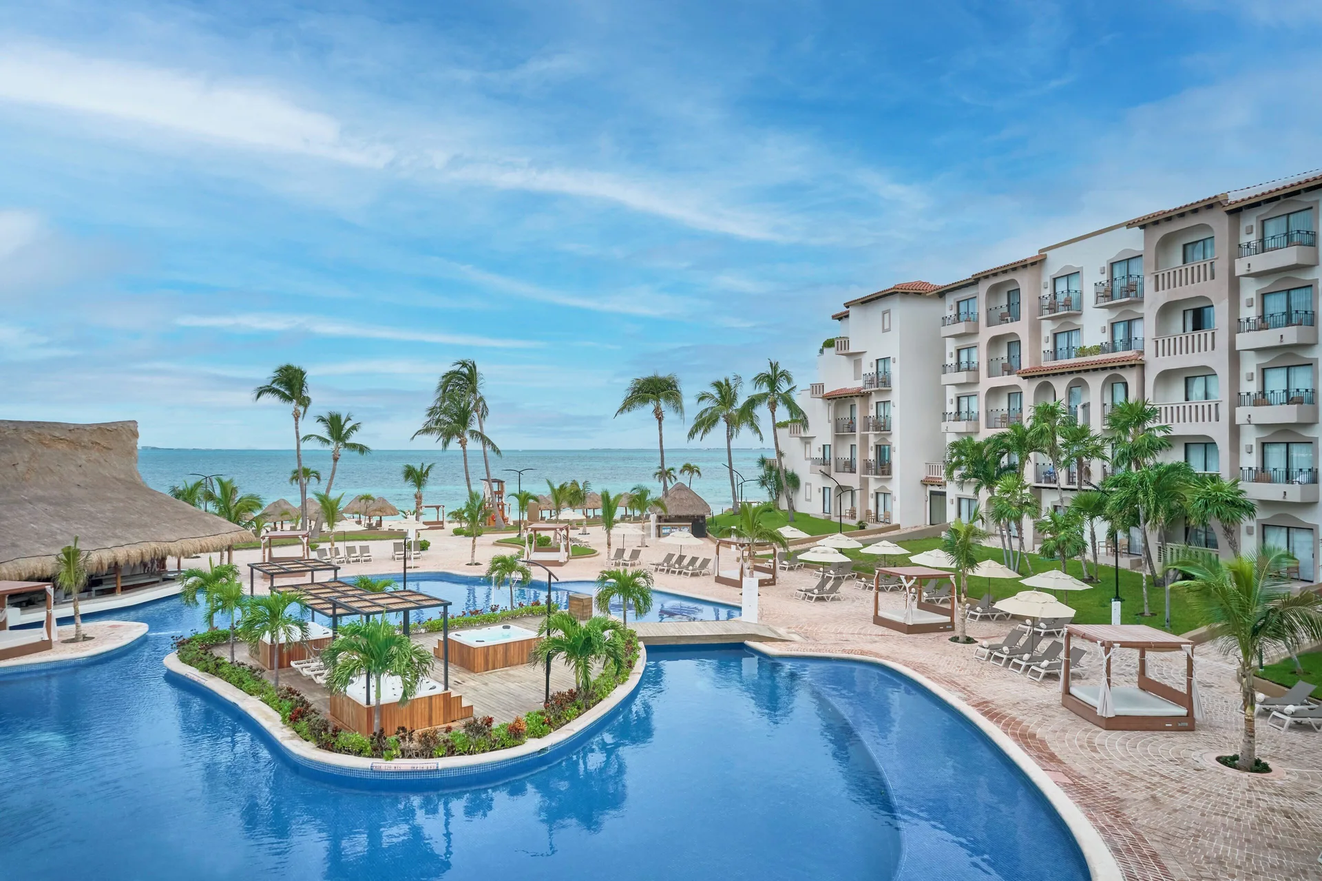 Resort pool area with ocean, palms, and cabanas at Fiesta Americana Cancun Villas.