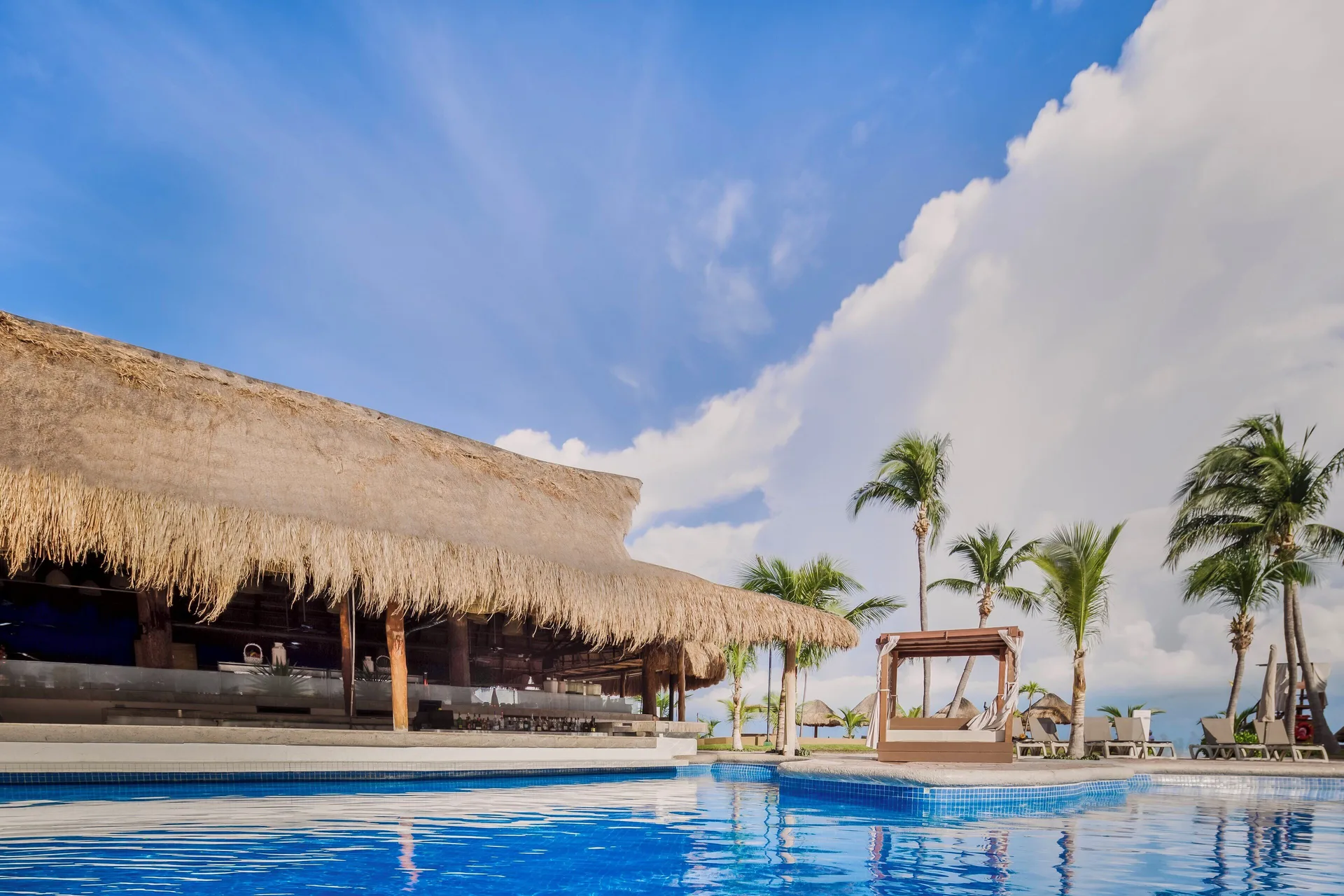 Pool beside a thatched bar and palm trees at Fiesta Americana Cancun Villas.