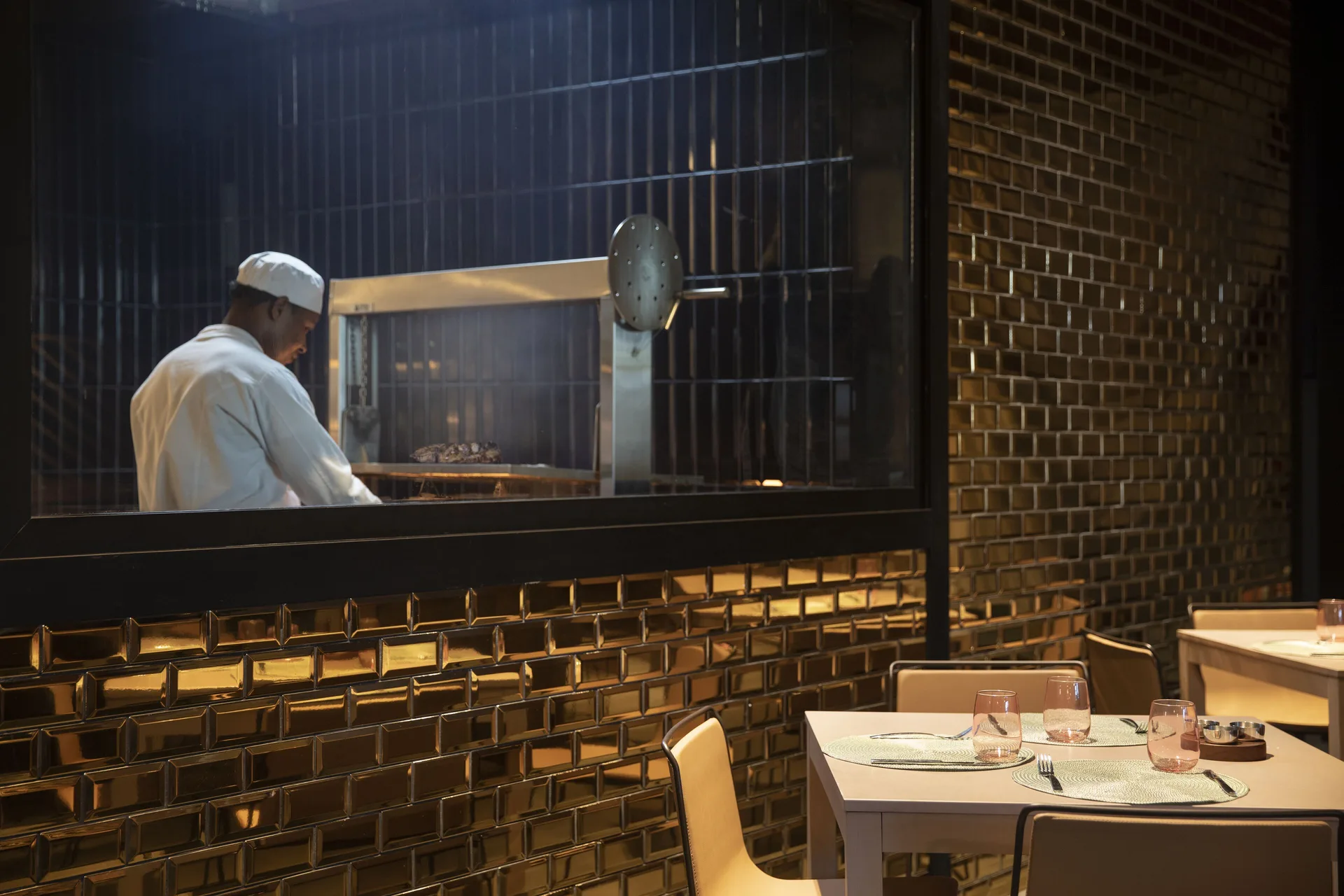 Chef works behind a glassed-in grill beside set tables at Finest Punta Cana.