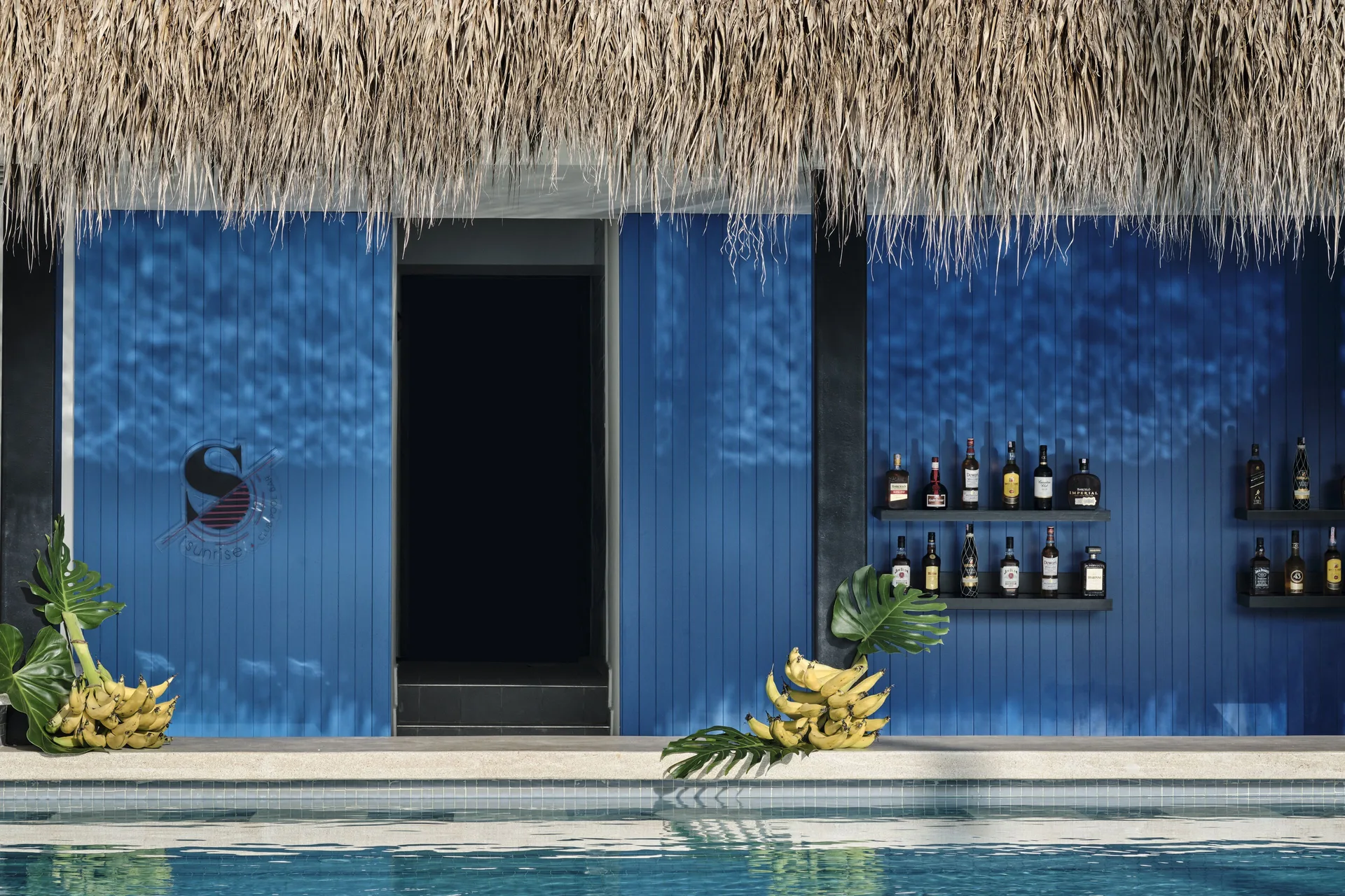 Blue poolside bar wall with shelves of bottles and bananas at Finest Punta Cana.