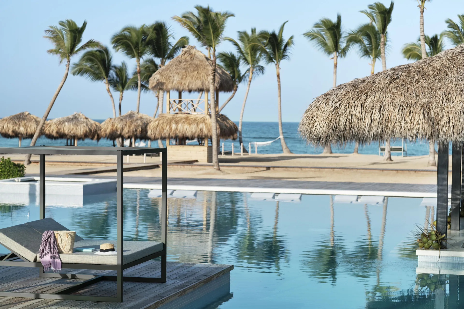 Beachfront pool with daybed, palms, and ocean at Finest Punta Cana.
