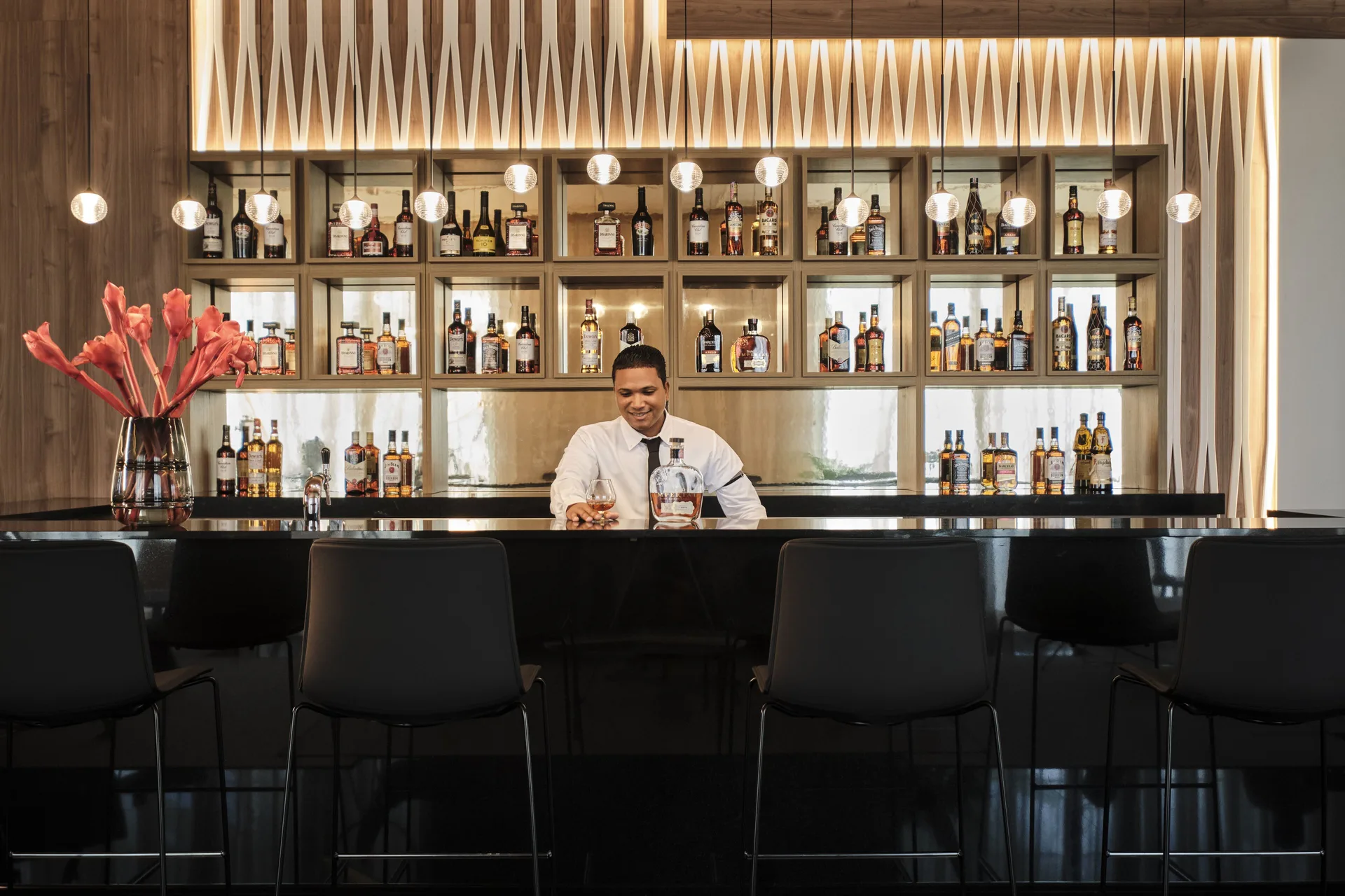 Bartender behind a glossy bar with illuminated bottle shelves at Finest Punta Cana.