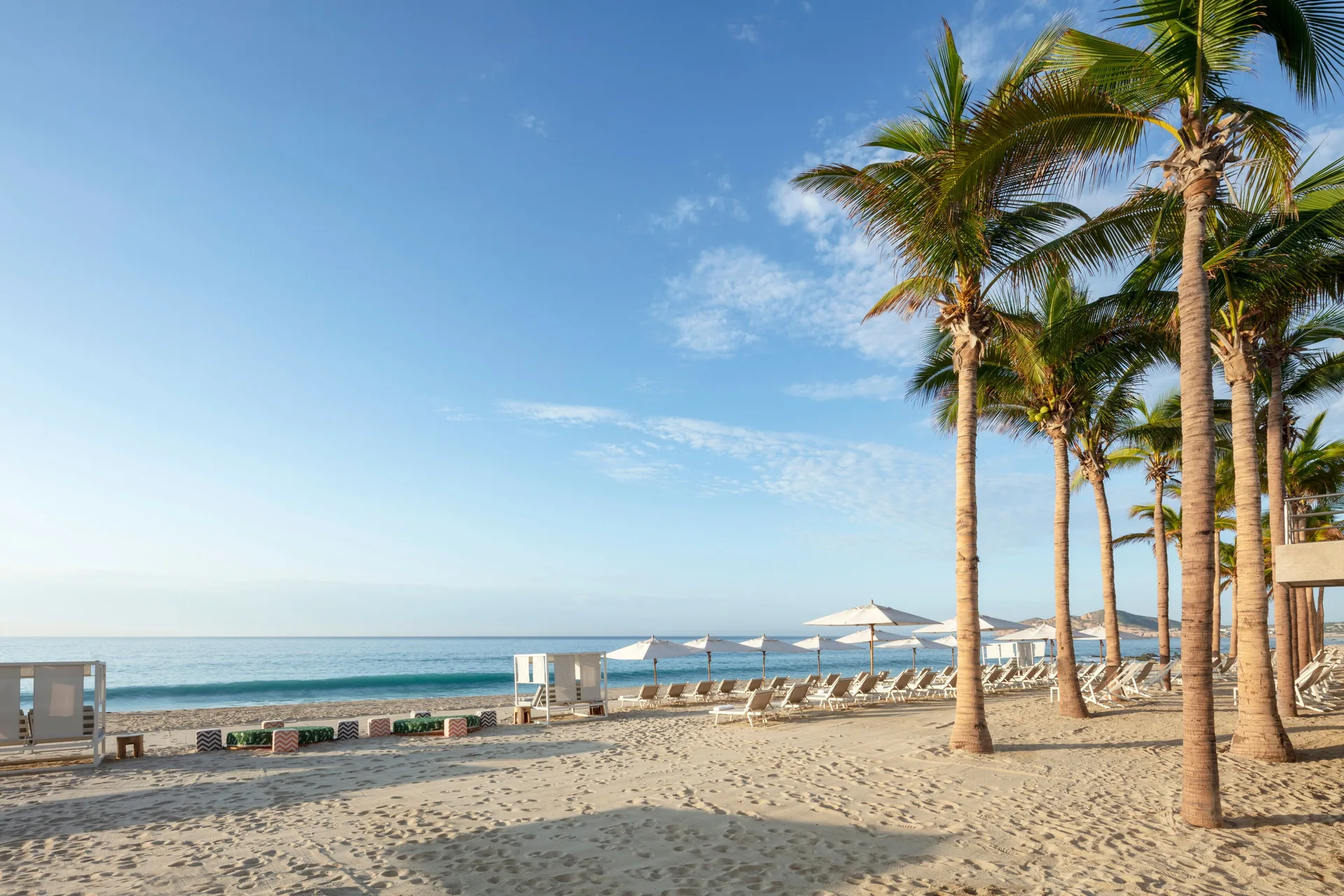Beach loungers, umbrellas, palm trees, and calm ocean at Garza Blanca Los Cabos.