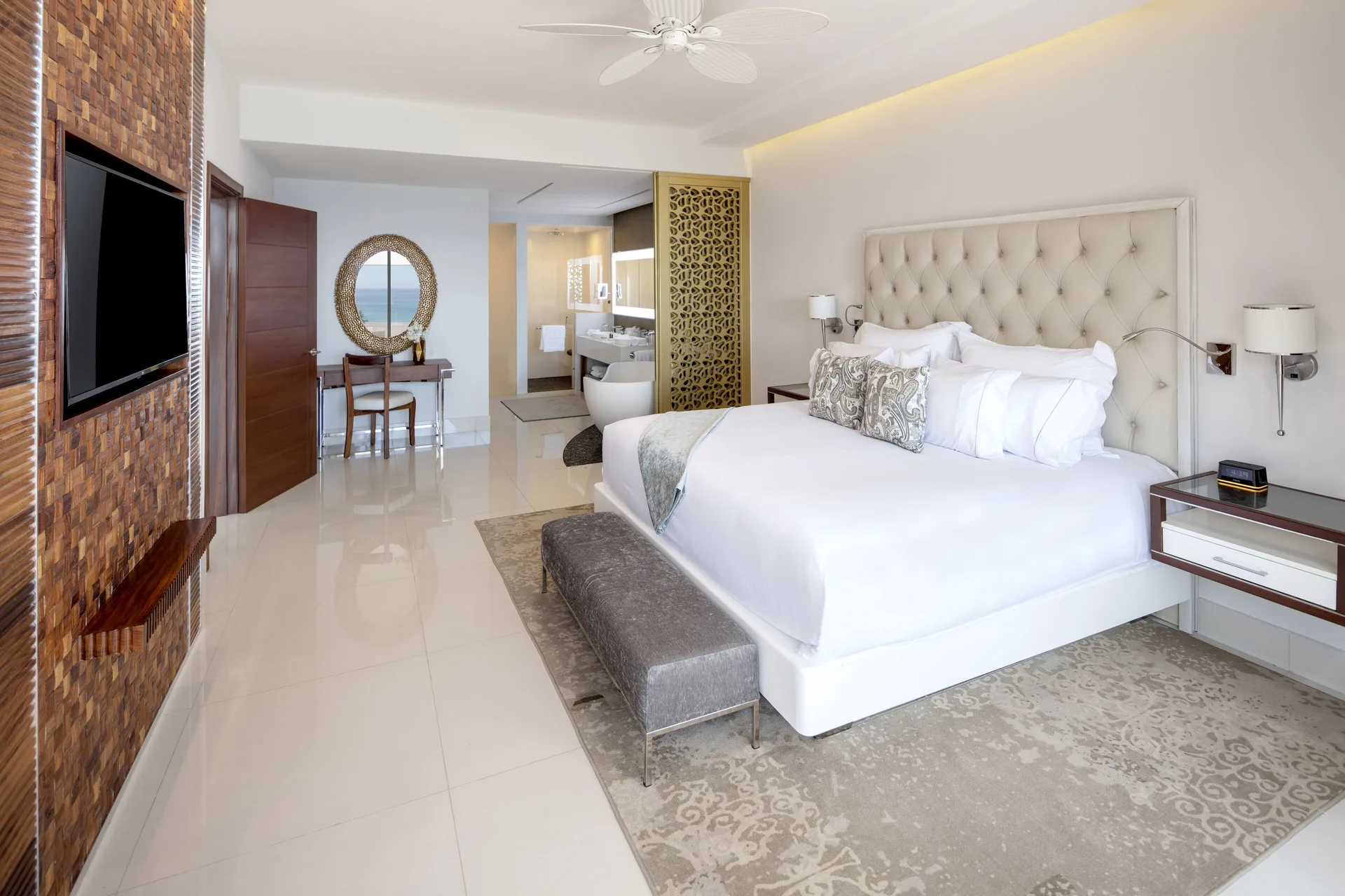 King bedroom with TV wall, bench, and ocean glimpse at Garza Blanca Los Cabos.