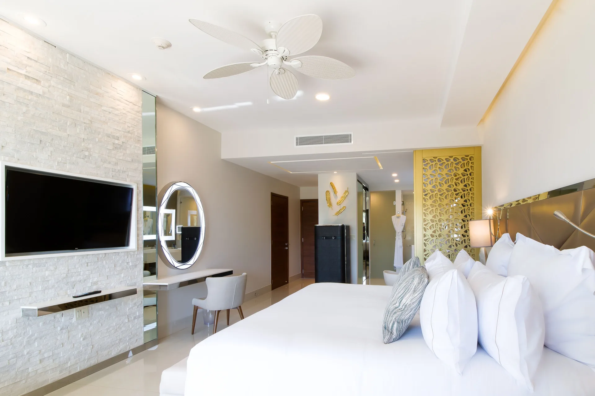 Junior Suite king bed with TV wall, round vanity mirror, and entry area at Garza Blanca Los Cabos.