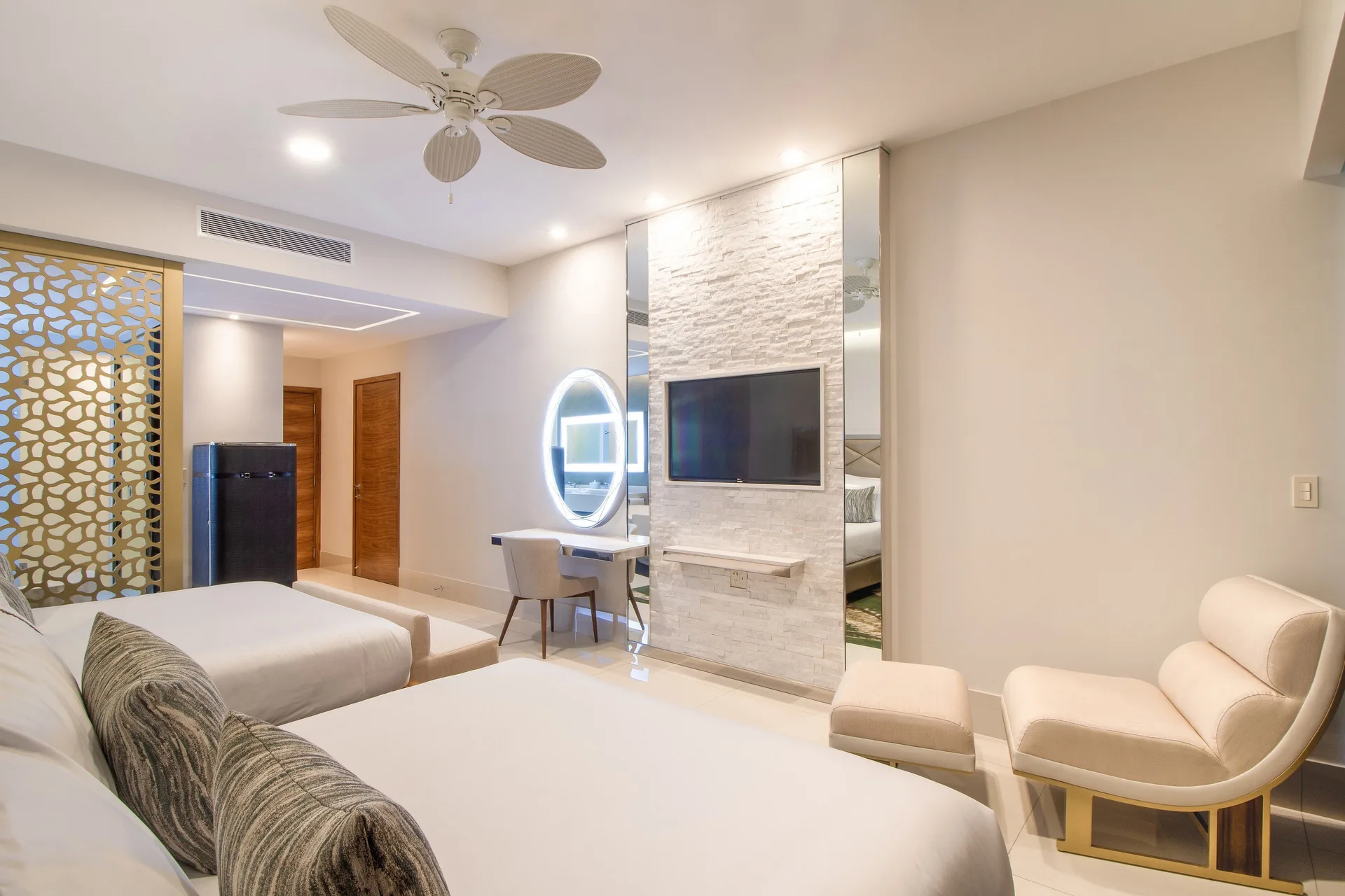 Junior Suite beds with lounge chair, TV wall, and illuminated vanity at Garza Blanca Los Cabos.