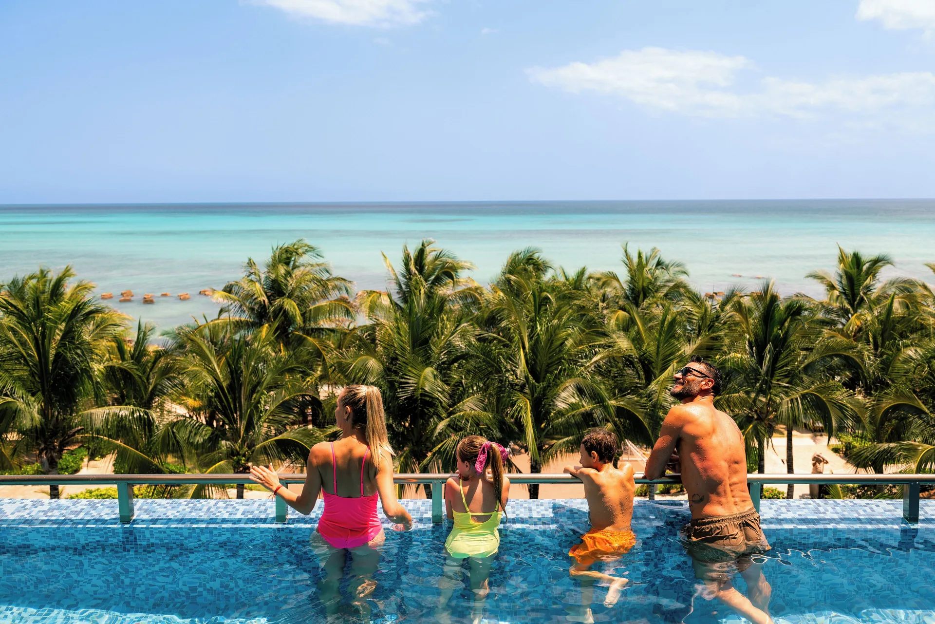 Family in an infinity-edge pool overlooking palms and the sea at Generations Riviera Maya.