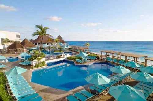 Pool deck with turquoise umbrellas beside the ocean at GR Solaris Caribe.