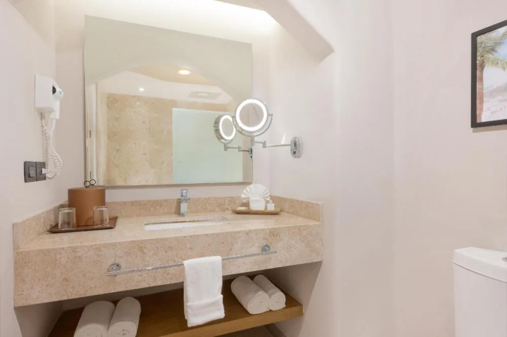 Deluxe Lagoon View bathroom vanity with large mirror, towels, sink, and lit makeup mirror at GR Solaris Caribe.