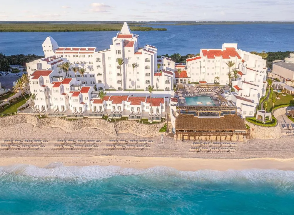 Aerial beachfront view of GR Solaris Caribe with white buildings, pool, beach loungers, and turquoise sea.
