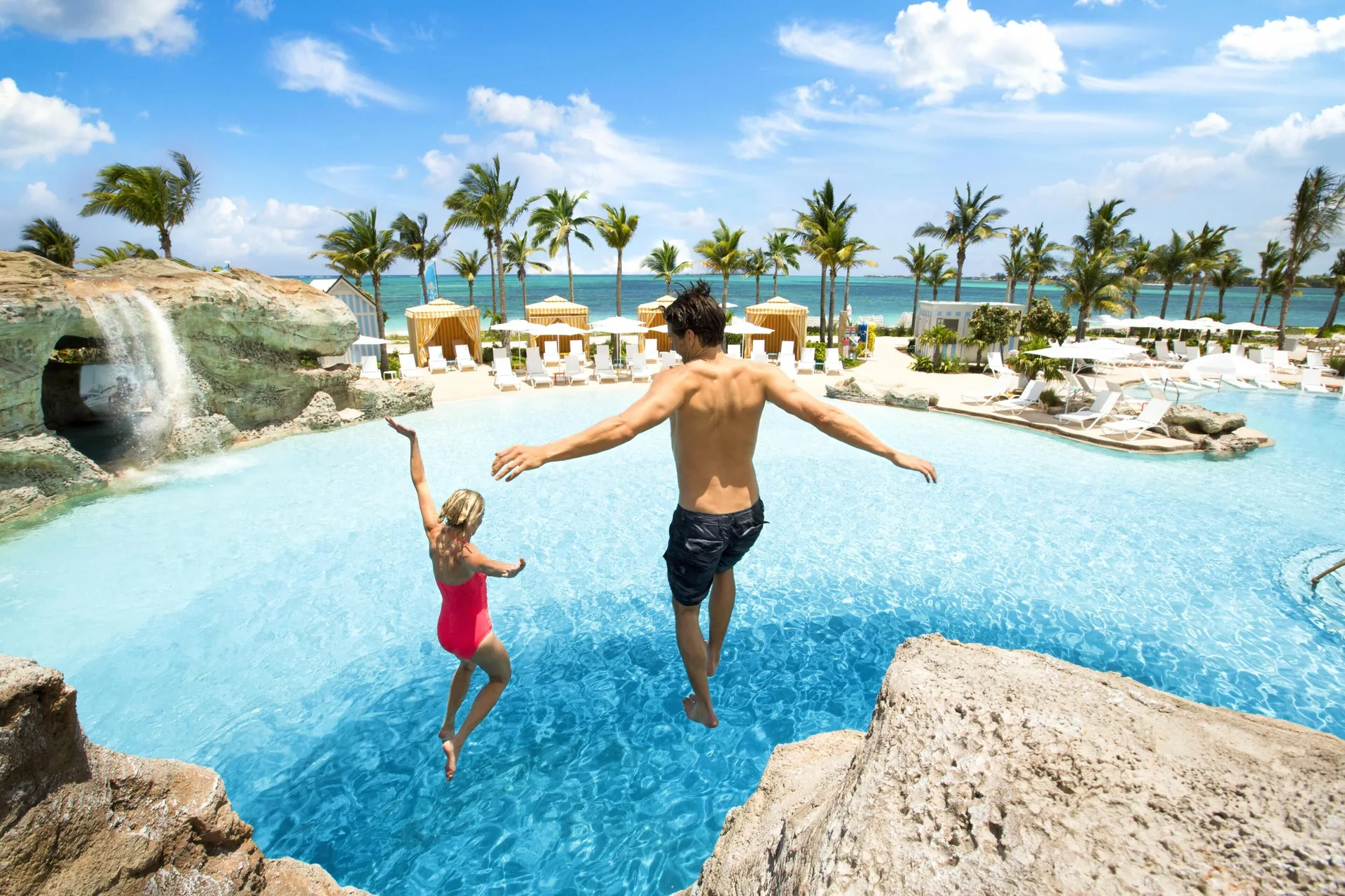 Two guests jumping into a resort pool by the beach at Grand Hyatt Baha Mar.