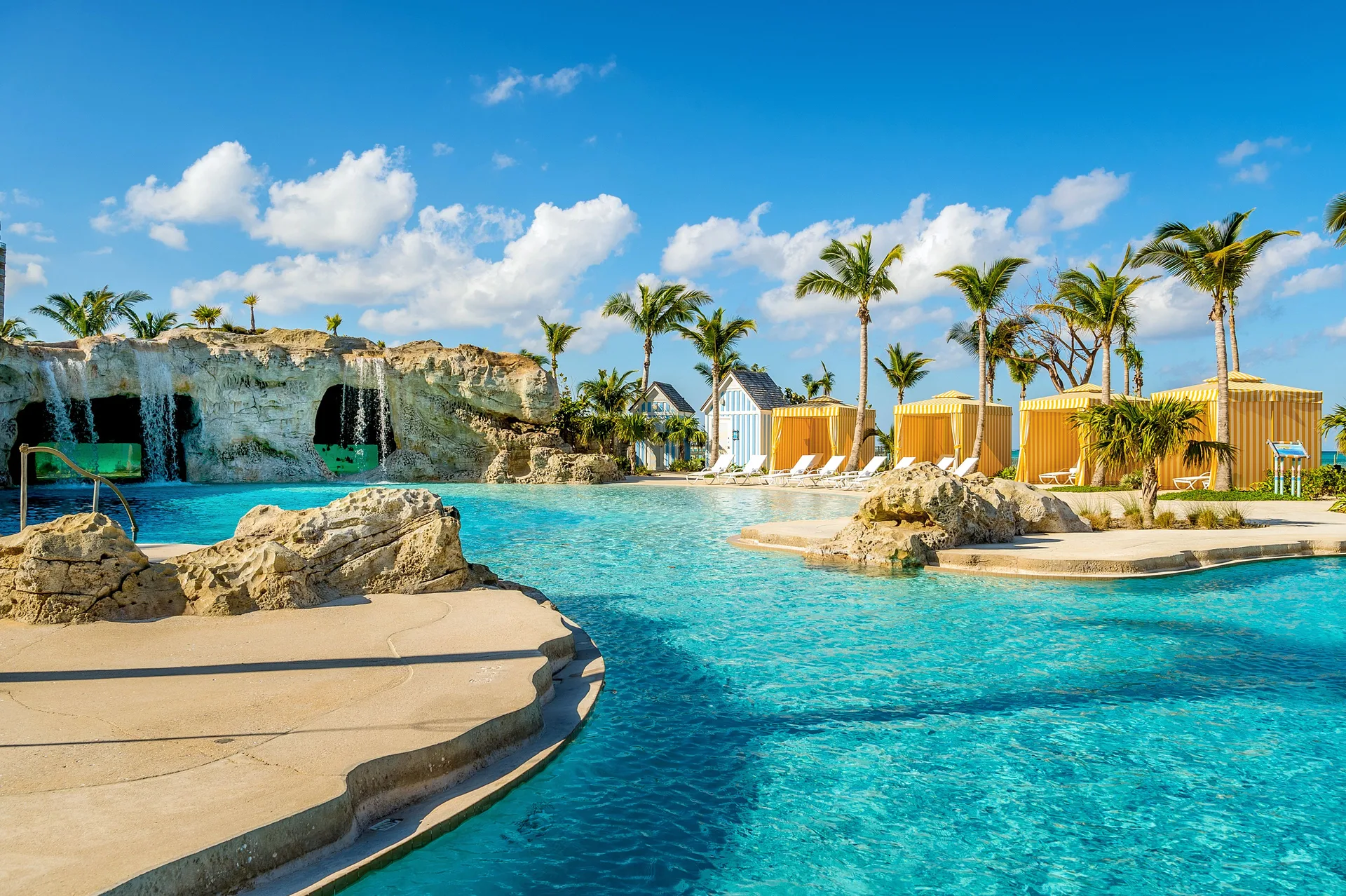 Lagoon-style pool with rock waterfalls, palms, and yellow cabanas at Grand Hyatt Baha Mar.