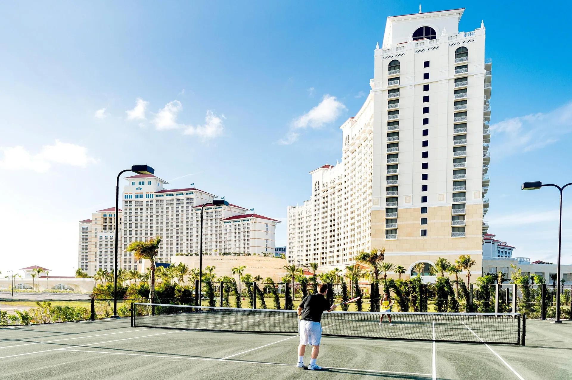 Guests play tennis on an outdoor court beside the hotel towers at Grand Hyatt Baha Mar.
