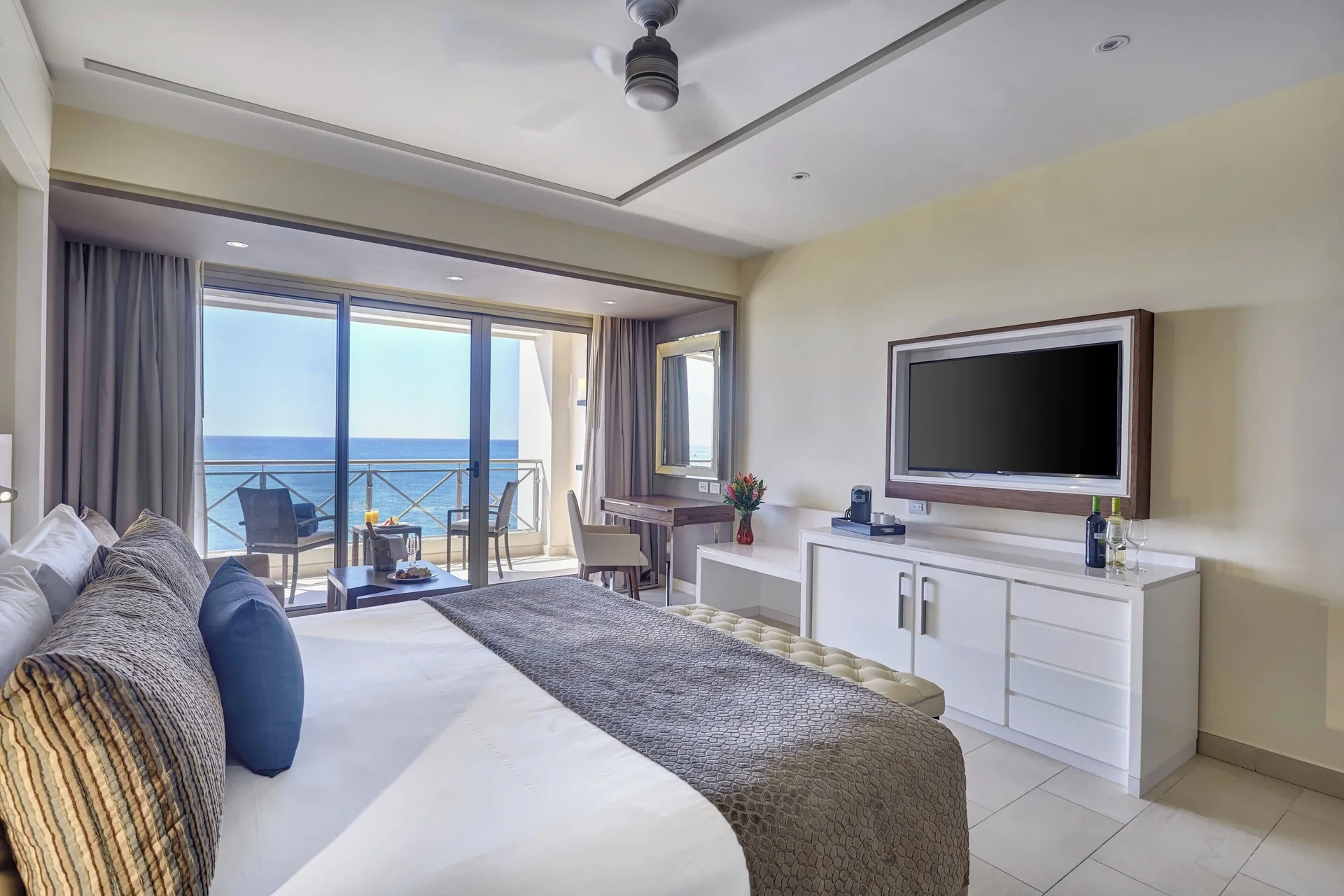 Sunset Ocean View Suite bedroom with king bed, TV, and ocean balcony at Grand Lido Negril Au-Naturel.