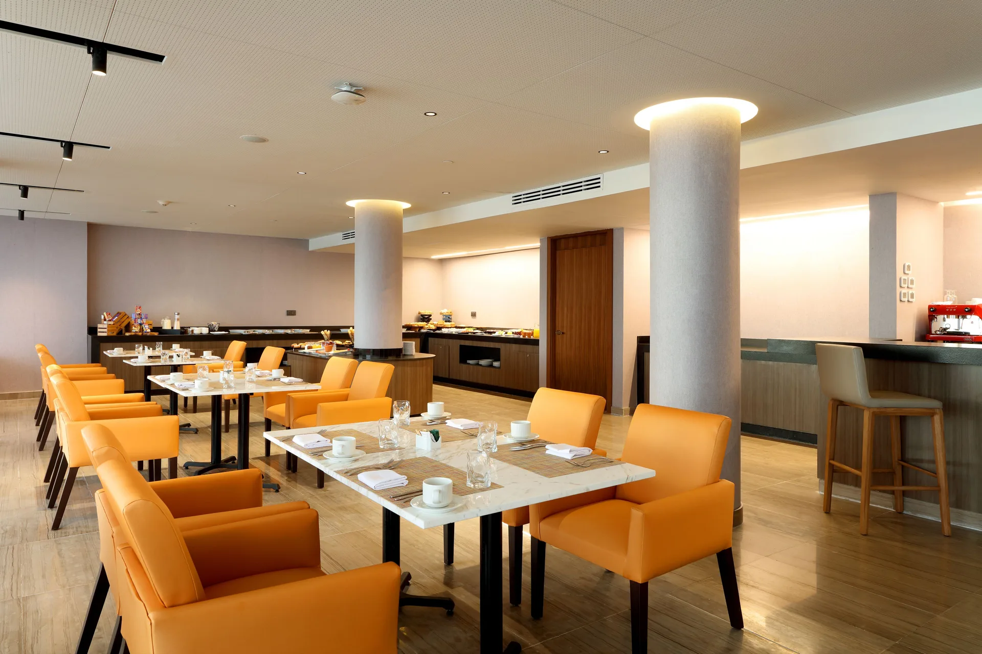 Dining room with orange chairs, set tables and buffet counters at Grand Palladium Select Costa Mujeres.