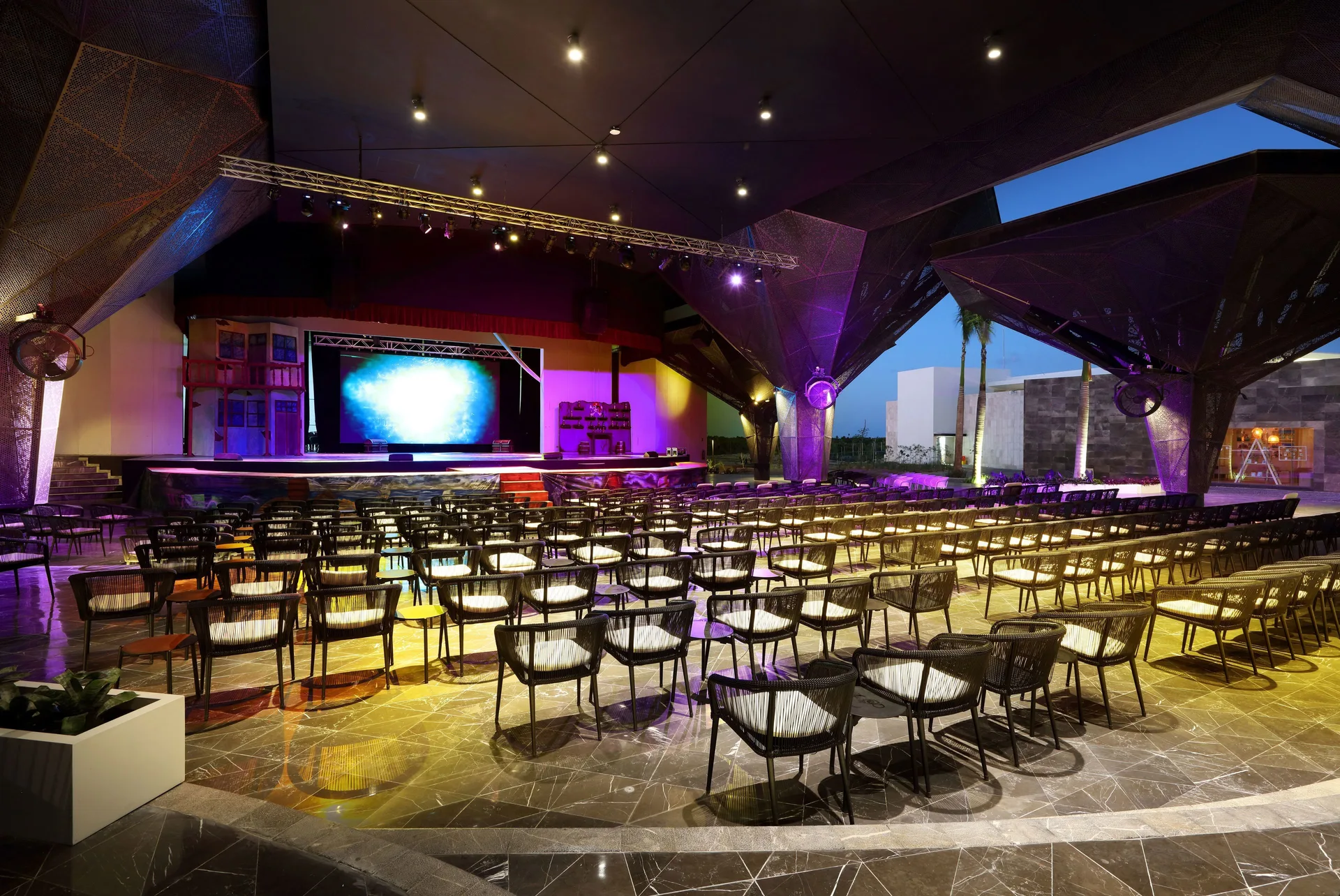 Outdoor theater with rows of chairs and a lit stage at Grand Palladium Select Costa Mujeres.