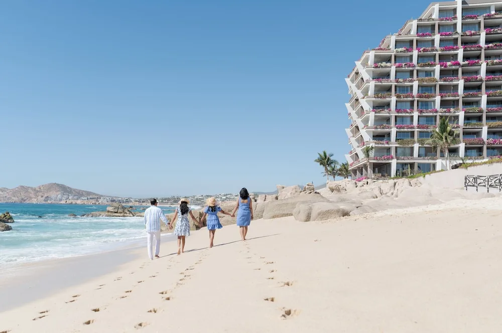 Family walking along the beach beside the resort building at Grand Velas Los Cabos.