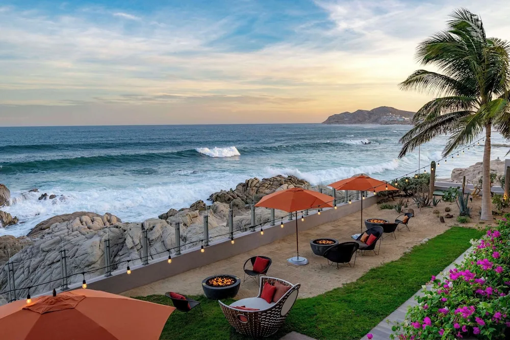 Coastal lawn with umbrellas, fire pits, and ocean waves at Grand Velas Los Cabos.