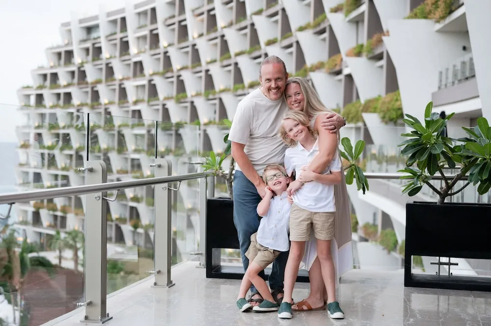 Family posing on a glass-railed balcony by guest room terraces at Grand Velas Los Cabos.