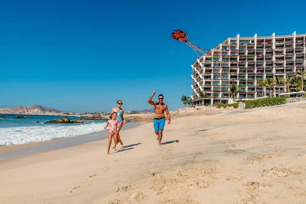 A family flies a kite on the beach by Grand Velas Los Cabos.
