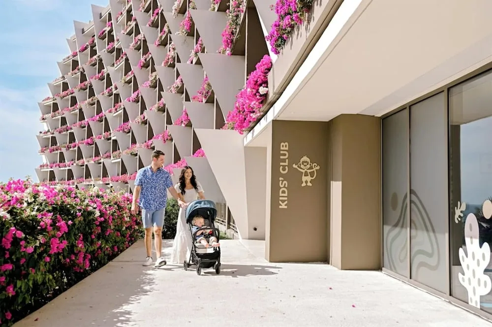 Family walking past the Kids' Club and flowered resort facade at Grand Velas Los Cabos.