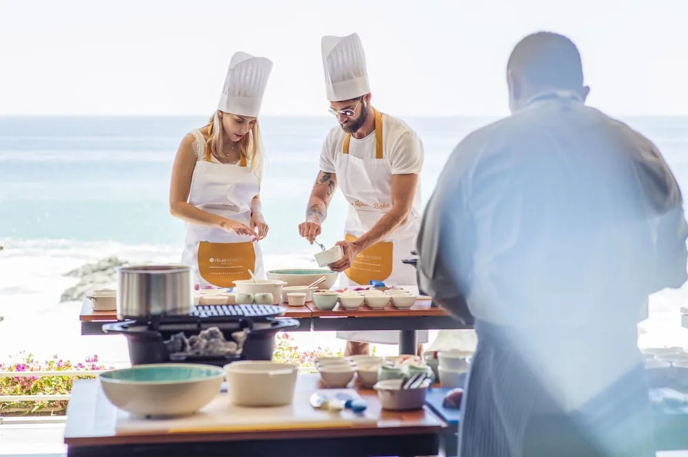 Cooking class by the ocean at Grand Velas Los Cabos with guests and a chef at prep tables.