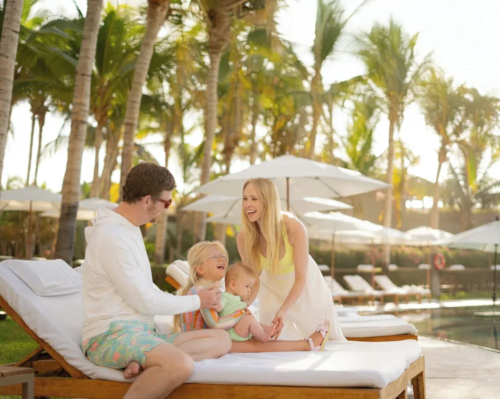 Family relaxing on a poolside daybed under palms at Grand Velas Los Cabos.