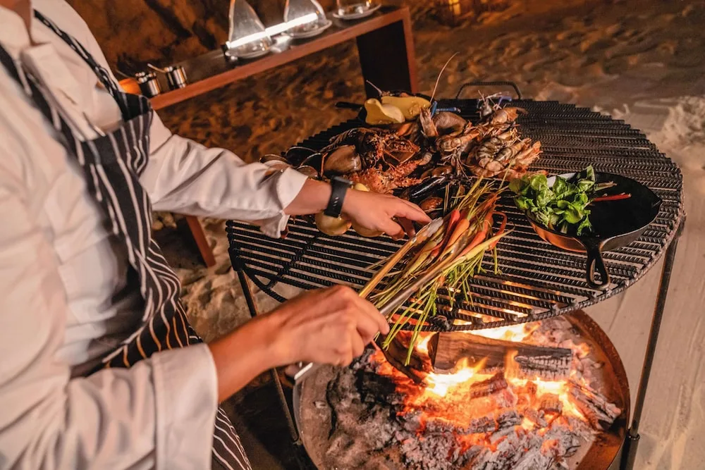 Chef grilling seafood and vegetables over an open fire at Grand Velas Los Cabos.