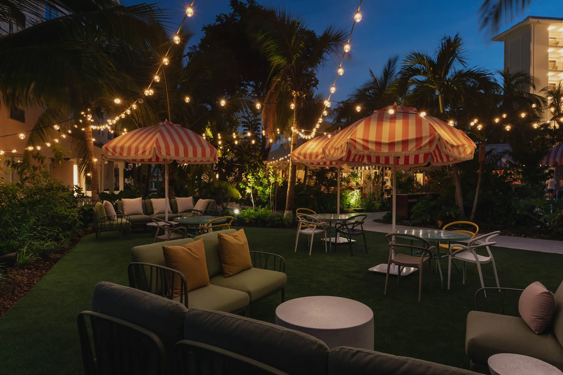 Evening courtyard seating at Hampton by Hilton Grand Cayman Seven Mile Beach with string lights and umbrellas.