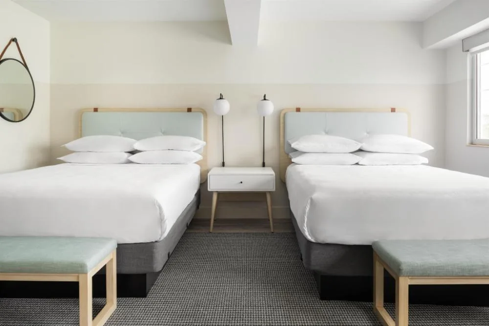 Two-bed guest room with benches and bedside table at Hampton by Hilton Grand Cayman Seven Mile Beach.