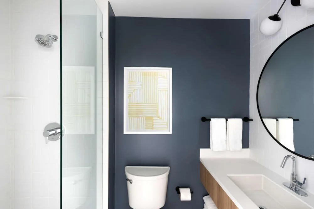 Studio bathroom with glass shower and round mirror at Hampton by Hilton Grand Cayman Seven Mile Beach.
