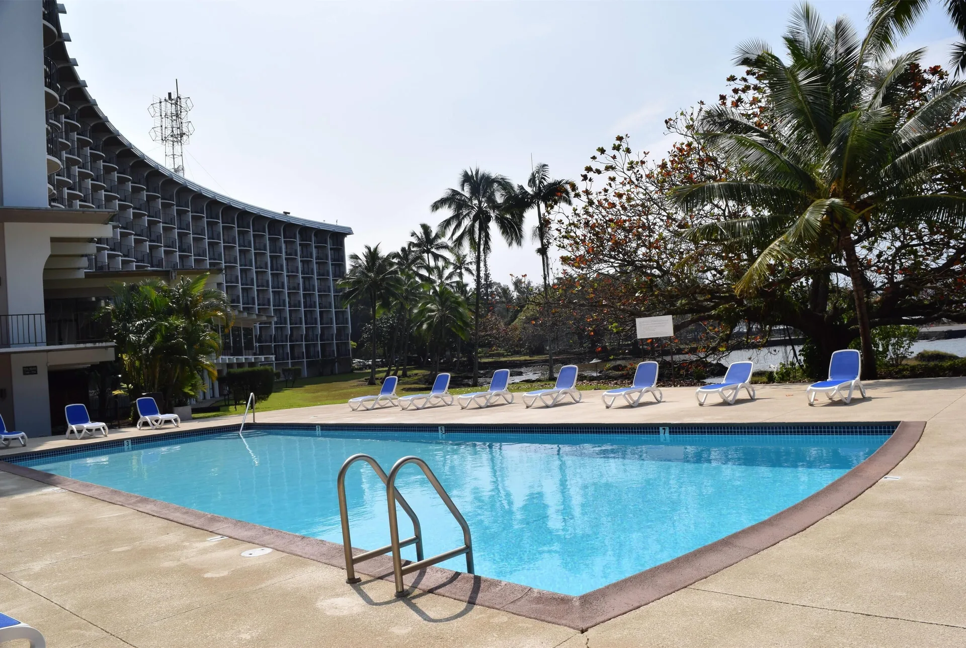 Pool deck with lounge chairs, palms, and hotel balconies at Hilo Hawaiian Hotel.