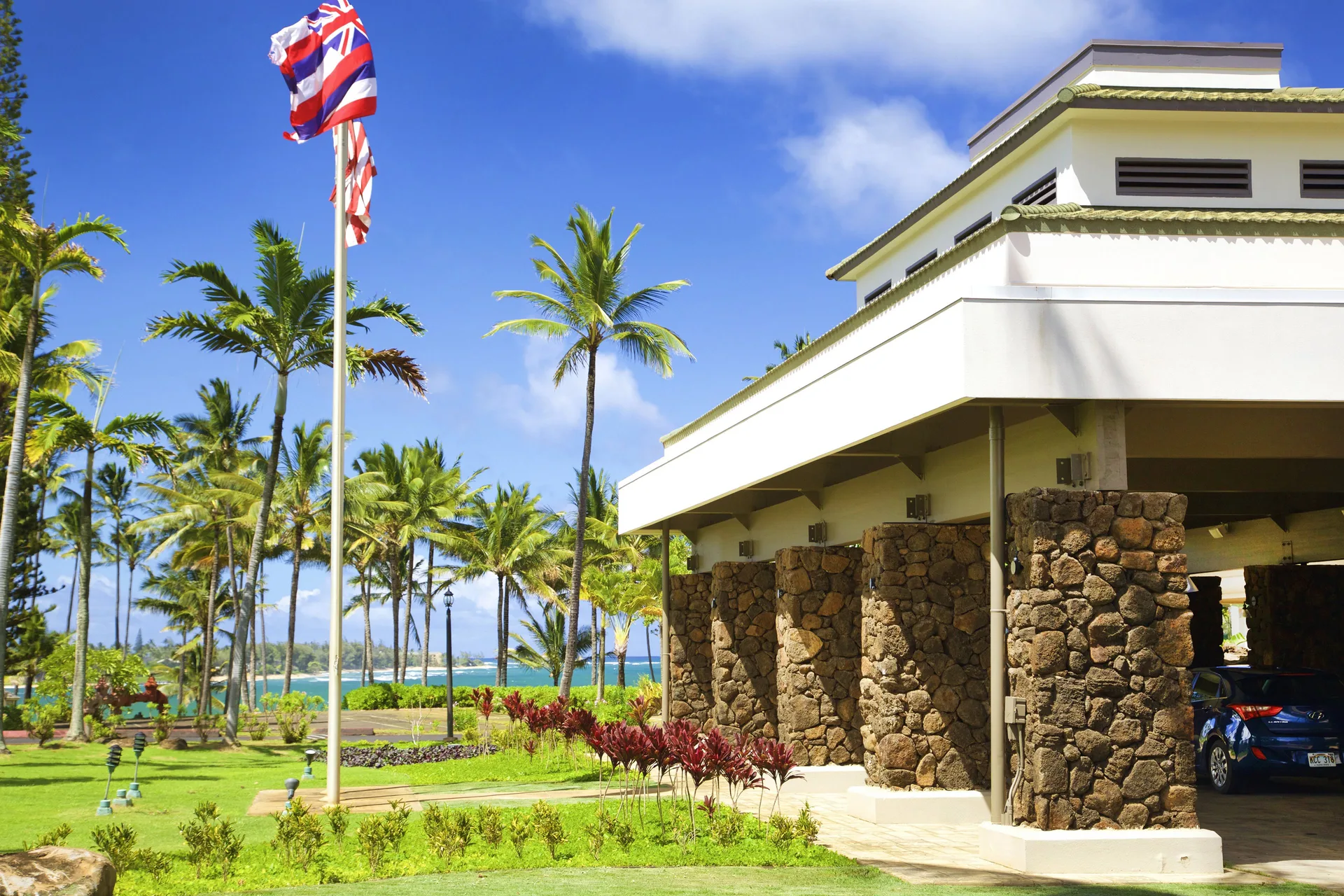 Entrance exterior with stone columns and ocean beyond at Hilton Garden Inn Kauai Wailua Bay.