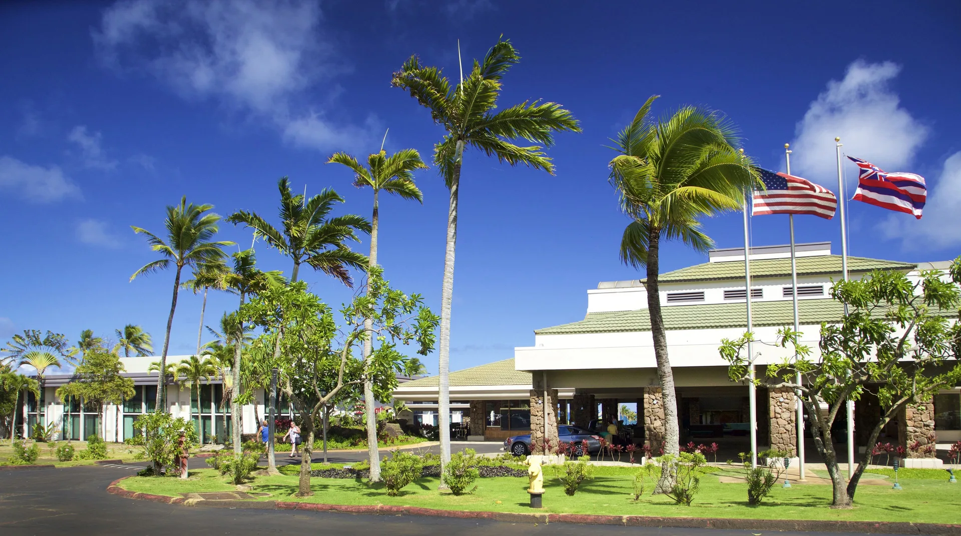 Front entrance with flags and palms at Hilton Garden Inn Kauai Wailua Bay.