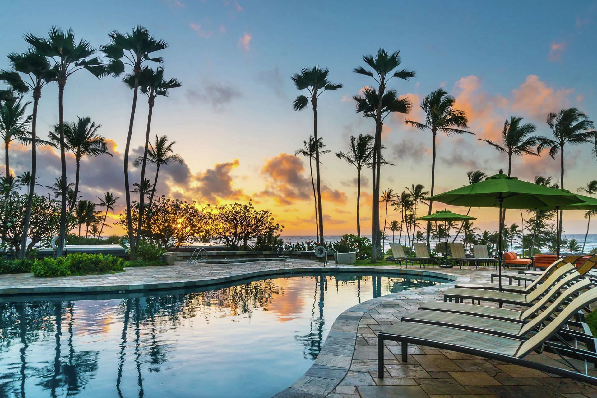 Sunset pool with palm trees and ocean beyond at Hilton Garden Inn Kauai Wailua Bay.