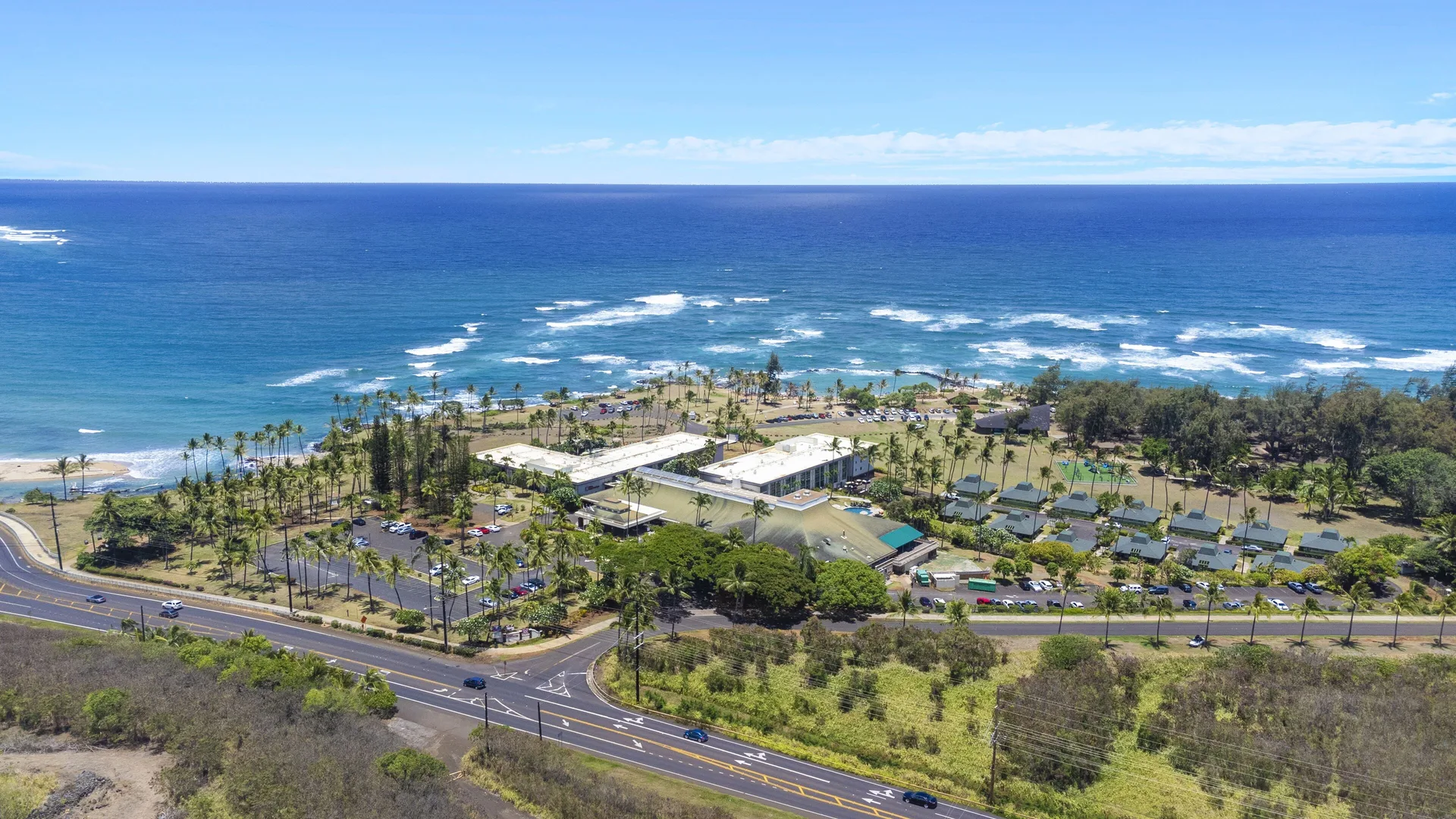 Wide aerial view of the resort, road, and ocean at Hilton Garden Inn Kauai Wailua Bay.