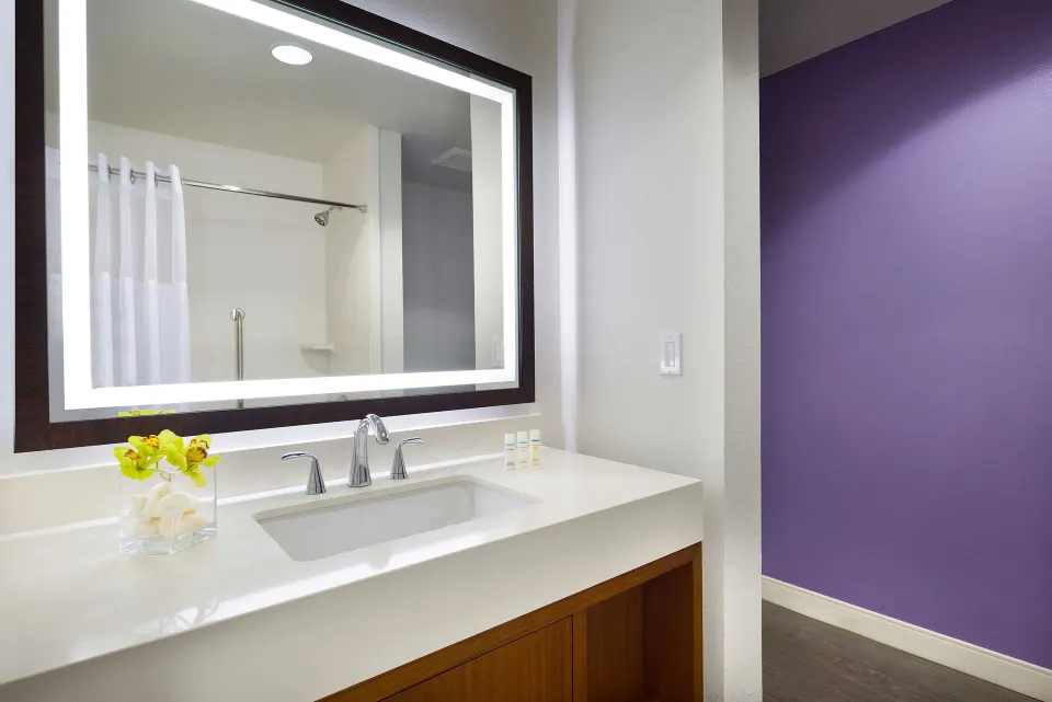 Cottage vanity with lighted mirror, sink, and purple accent wall at Hilton Garden Inn Kauai Wailua Bay.