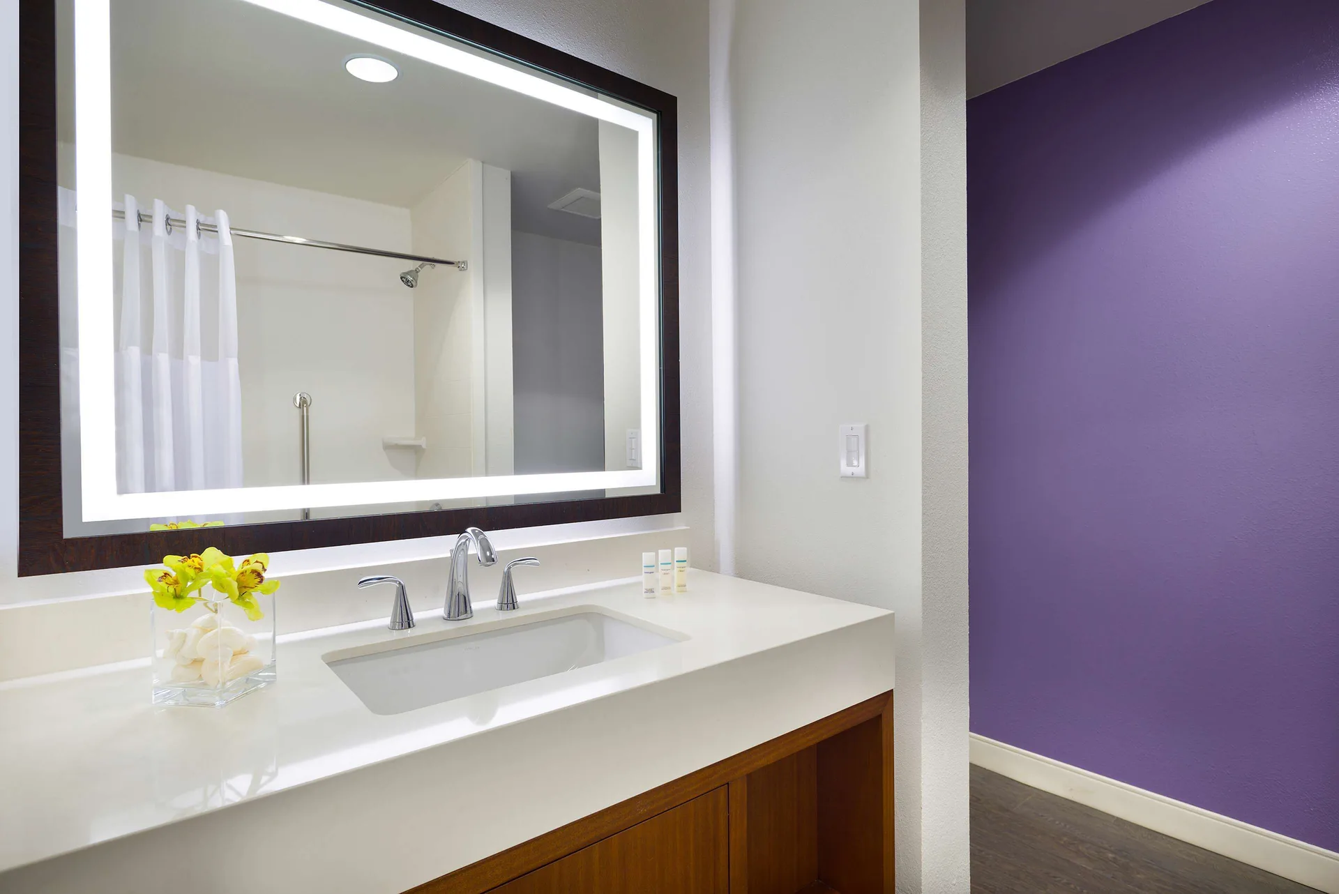 Cottage vanity with lighted mirror, sink, and purple accent wall at Hilton Garden Inn Kauai Wailua Bay.