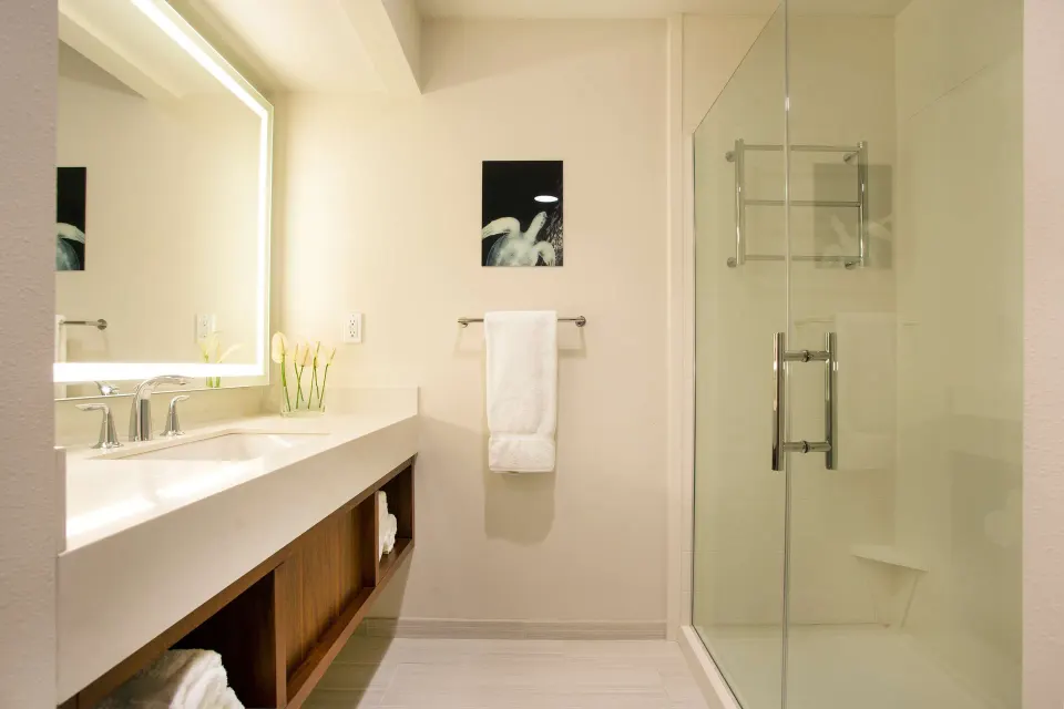Cottage bathroom with illuminated mirror, vanity, and glass shower at Hilton Garden Inn Kauai Wailua Bay.