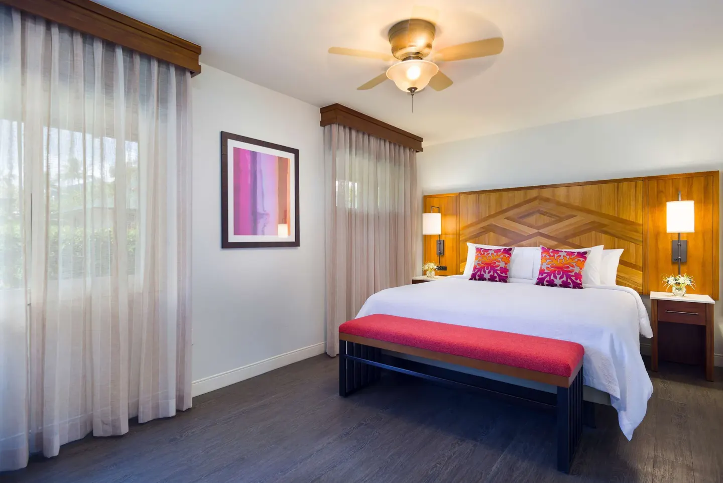 Cottage bedroom with a king bed, sheer curtains, and wood headboard at Hilton Garden Inn Kauai Wailua Bay.
