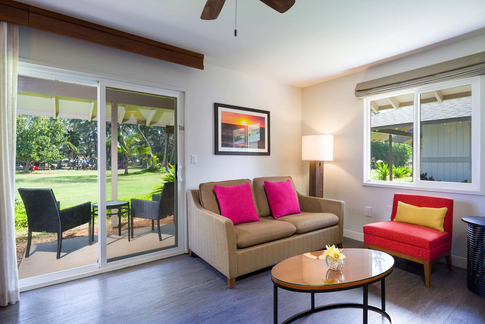 Cottage living room with sofa, red chair, and patio doors at Hilton Garden Inn Kauai Wailua Bay.