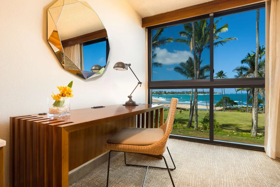 Ocean view room desk and window at Hilton Garden Inn Kauai Wailua Bay overlooking palms and beach.