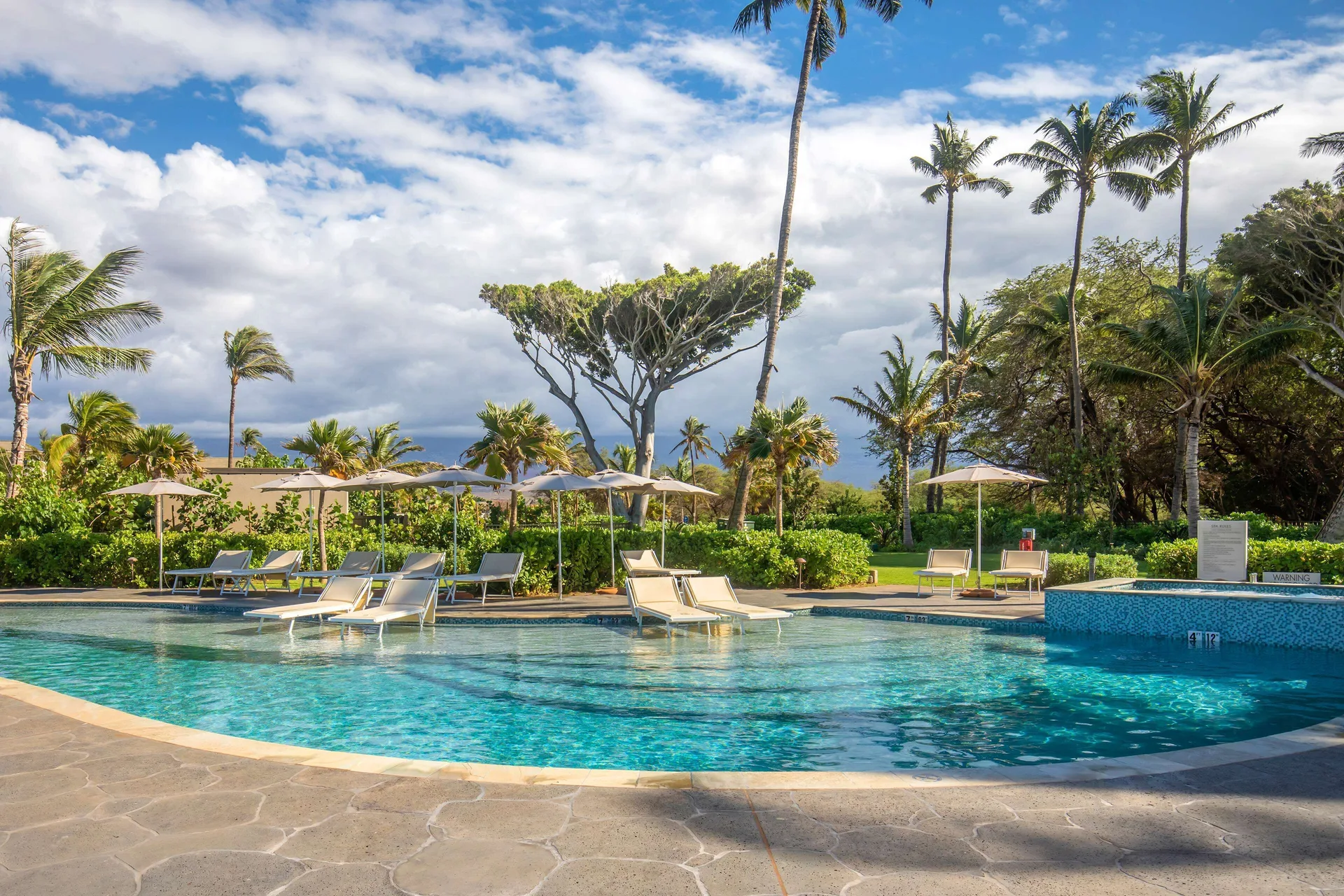 Pool loungers, umbrellas, and palms at Hilton Grand Vacations Club Maui Bay Villas.