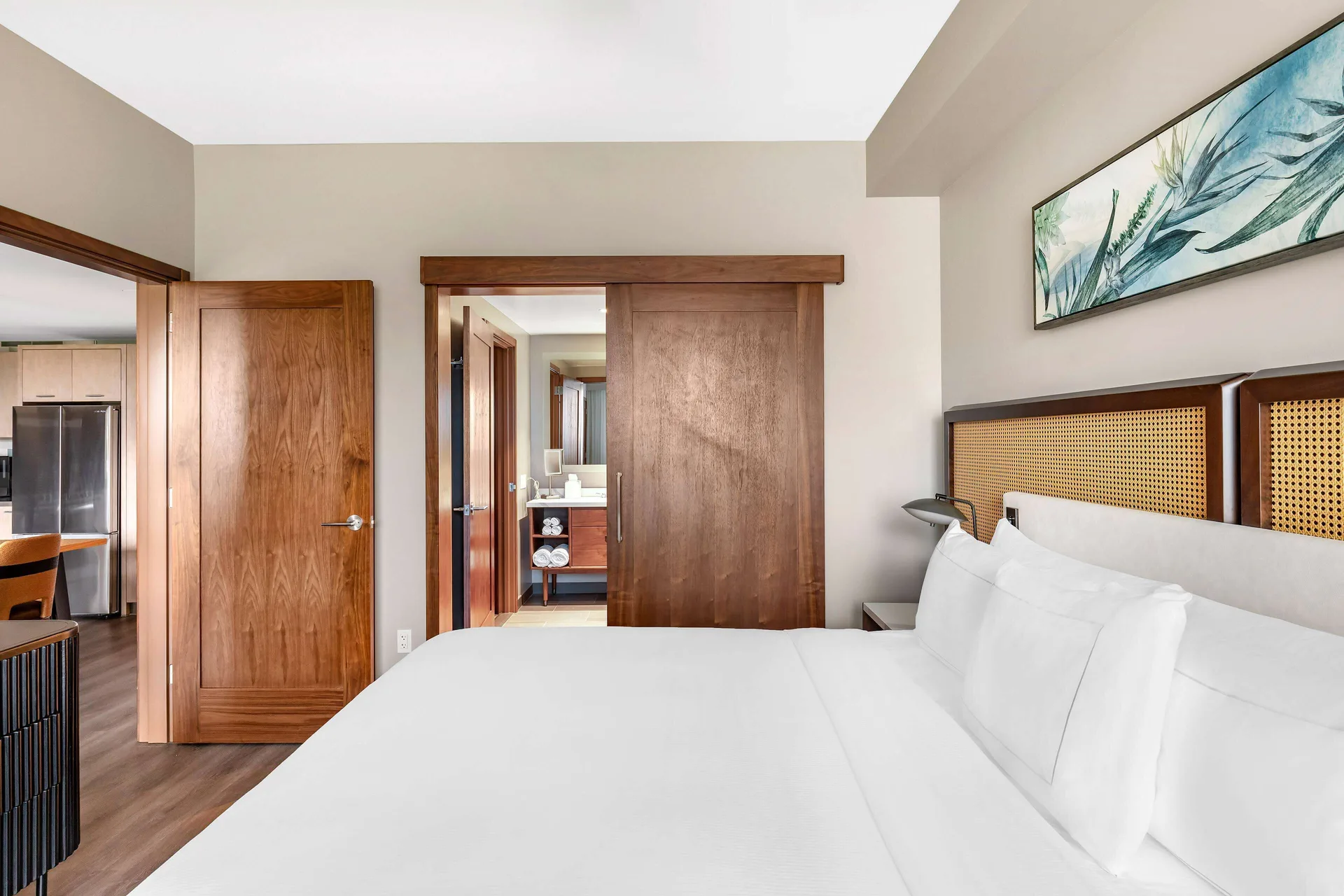 One-bedroom suite king bed with bathroom and kitchen beyond at Hilton Grand Vacations Club Maui Bay Villas.