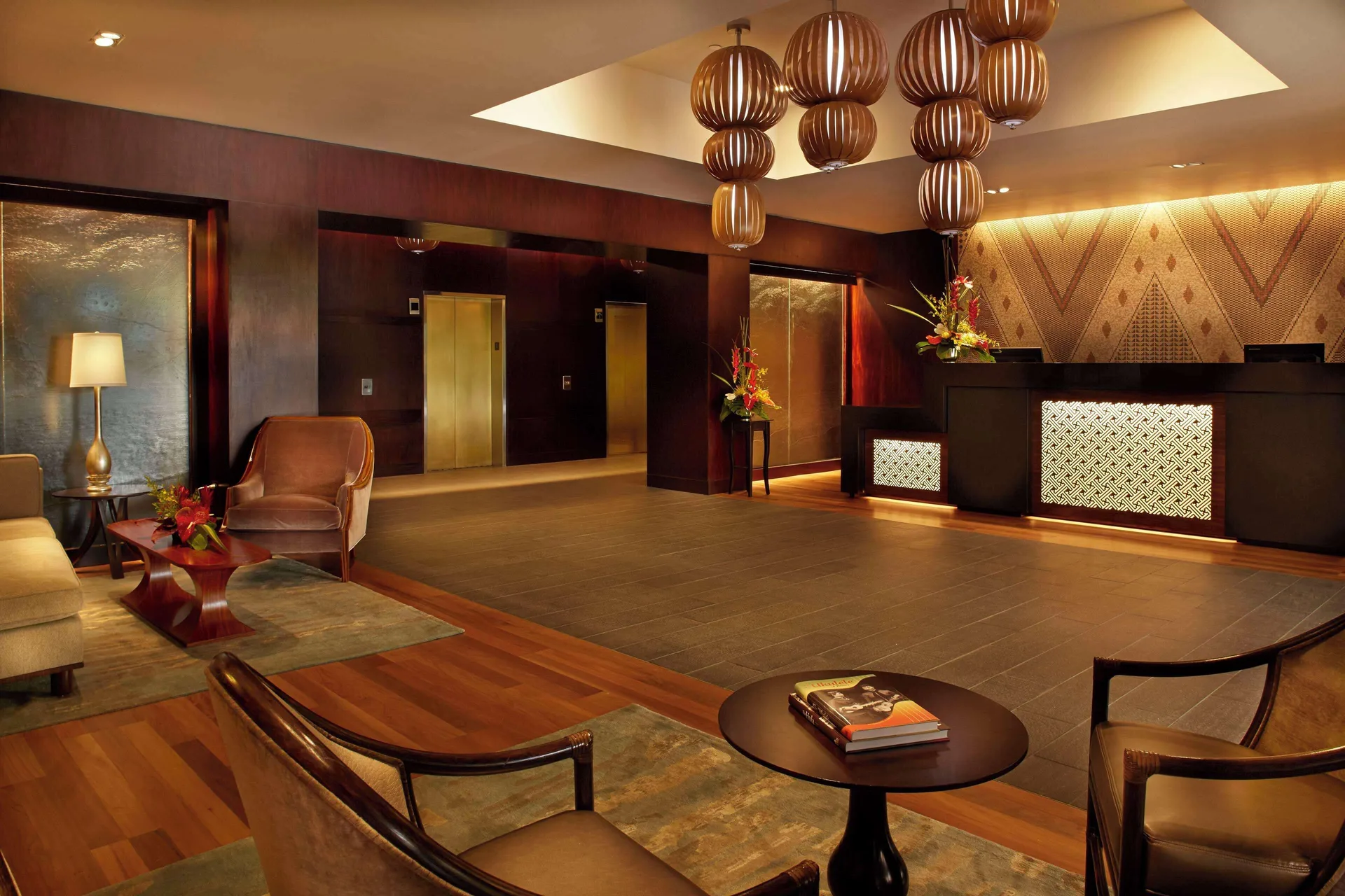 Warm wood lobby lounge with front desk, elevators, and pendant lights at Hilton Hawaiian Village Waikiki Beach Resort.