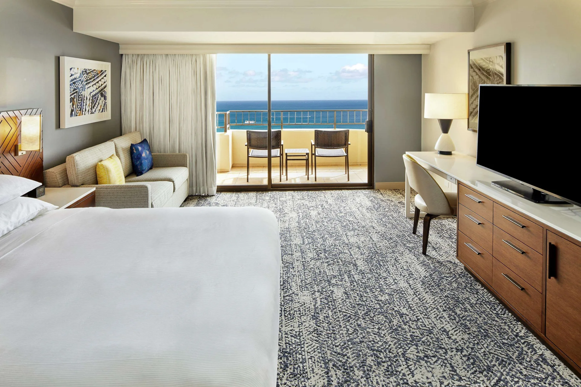 Ocean-view Tapa Collection room with bed, sofa, desk, TV, and balcony at Hilton Hawaiian Village Waikiki Beach Resort.