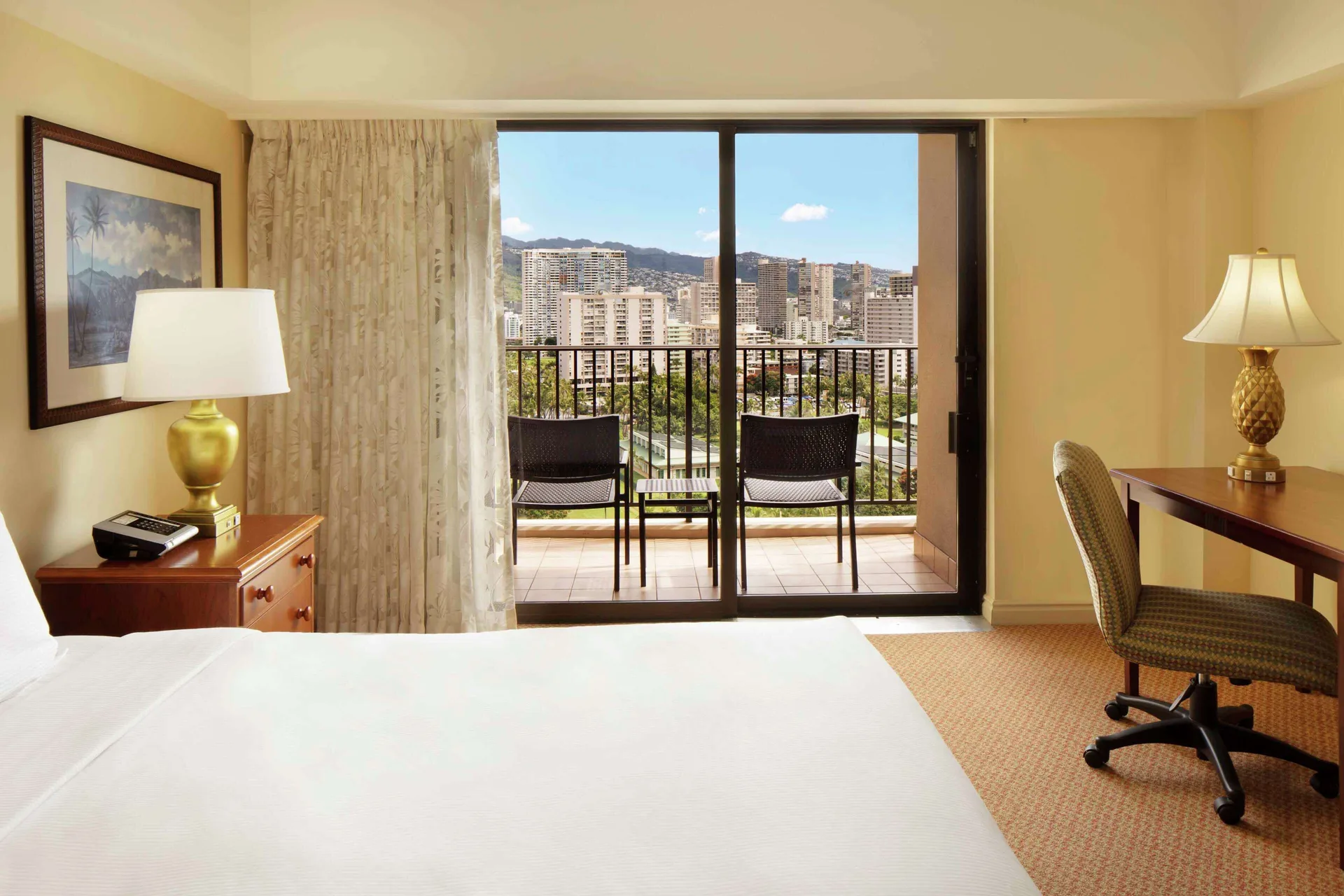 Resort view room with bed, lamps, desk, and balcony at Hilton Hawaiian Village Waikiki Beach Resort.