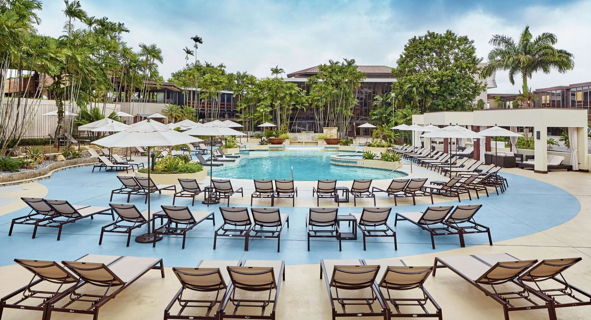 Daytime pool deck with umbrellas at Hilton Trinidad & Conference Centre.