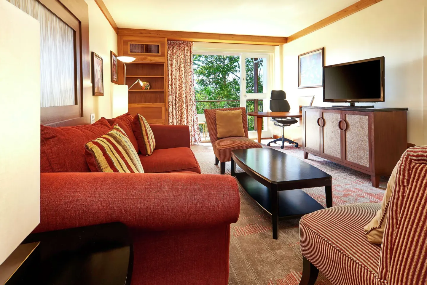 Living room with red sofa, desk, and TV at Hilton Trinidad & Conference Centre.